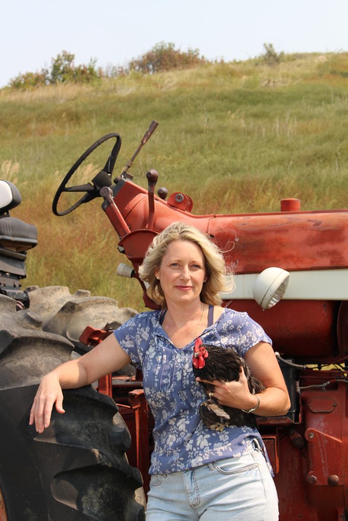 woman holding a black chicken leaning on an old red tractor.  About Season