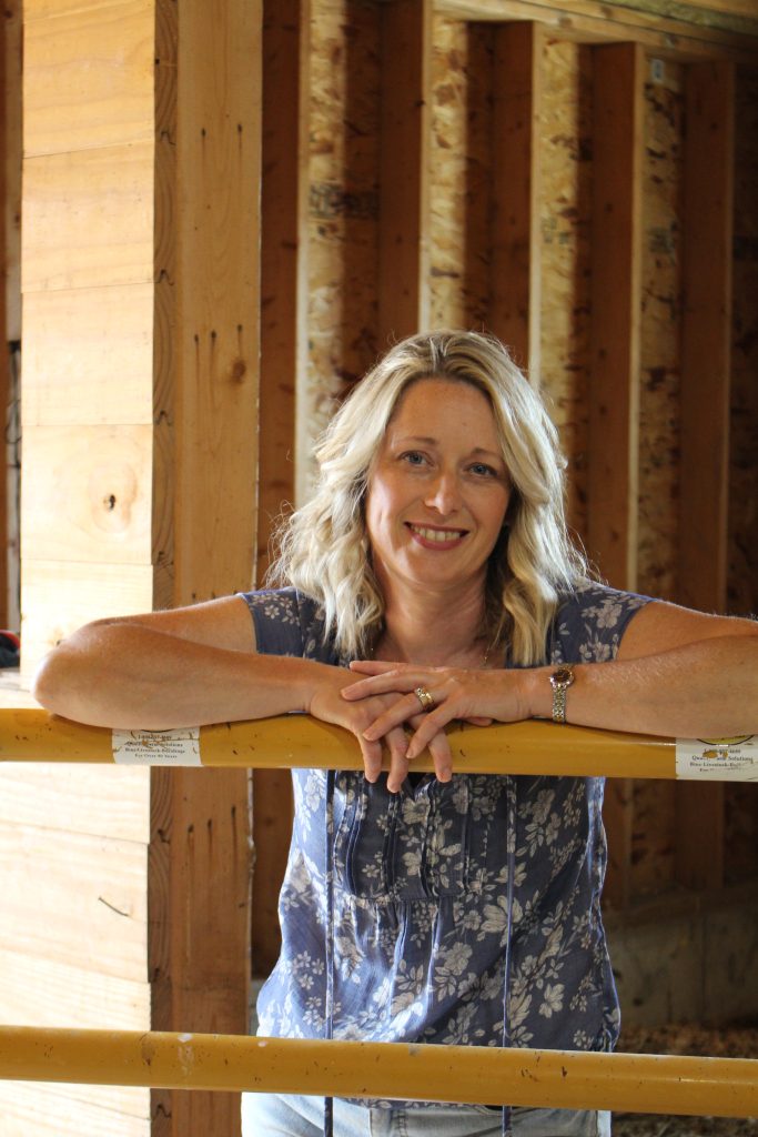 Woman leaning on yellow gate with wood in background. about Season